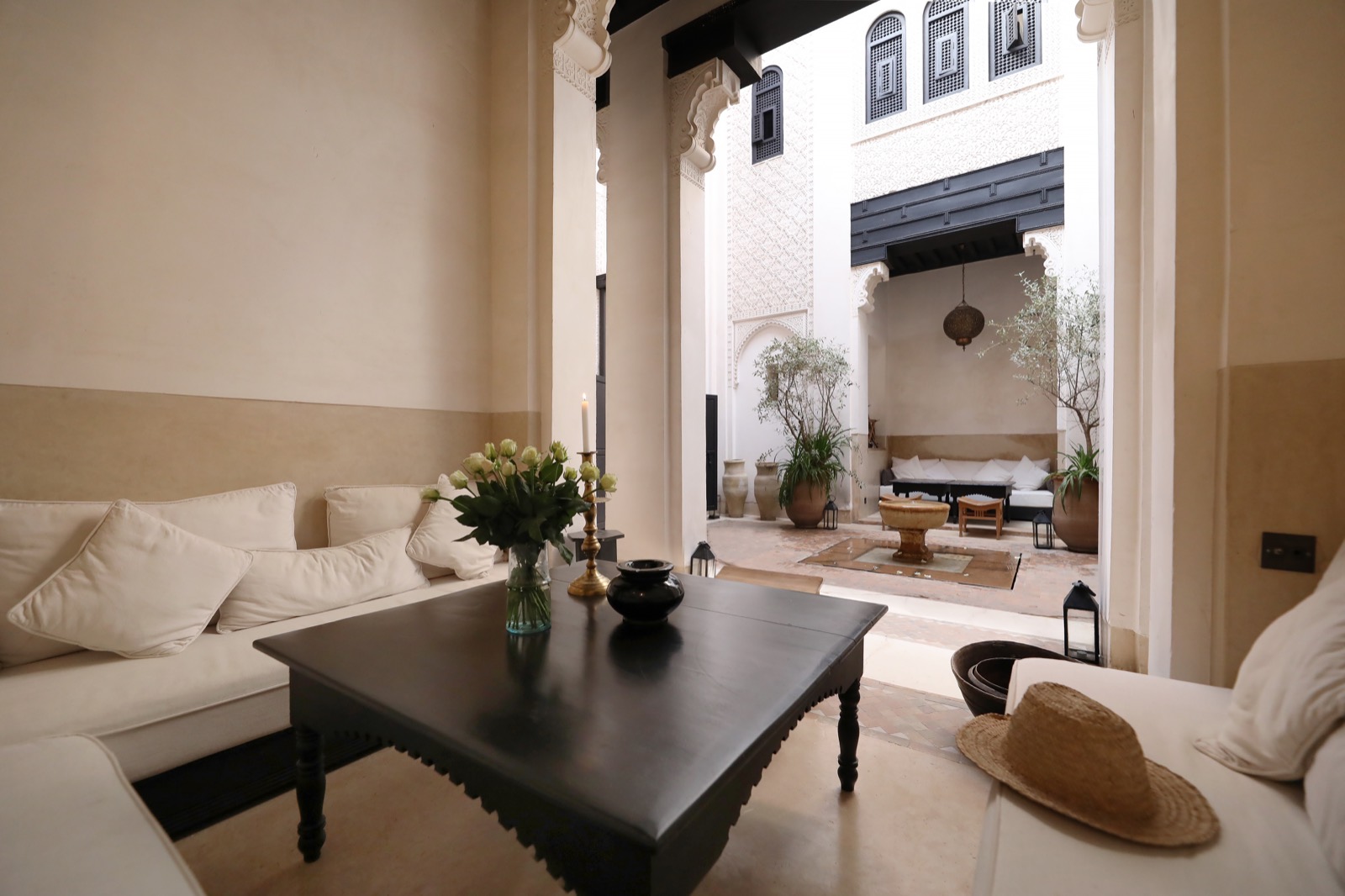 Le bhou du riad — banquettes blanches et table noire, ouvert par l’arche sur le patio et sa fontaine