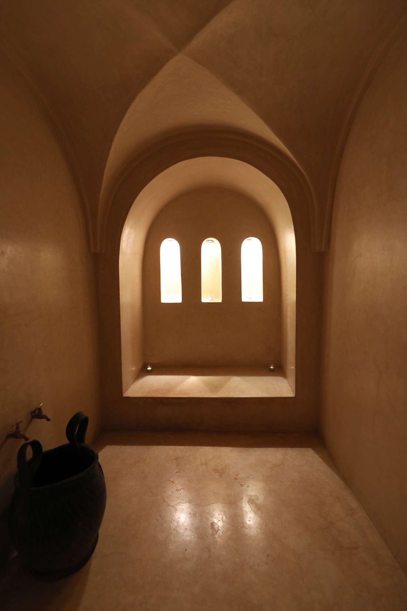 Le hammam voûté du riad en tadelakt, sa niche à trois arcs éclairés et son seau de cuivre