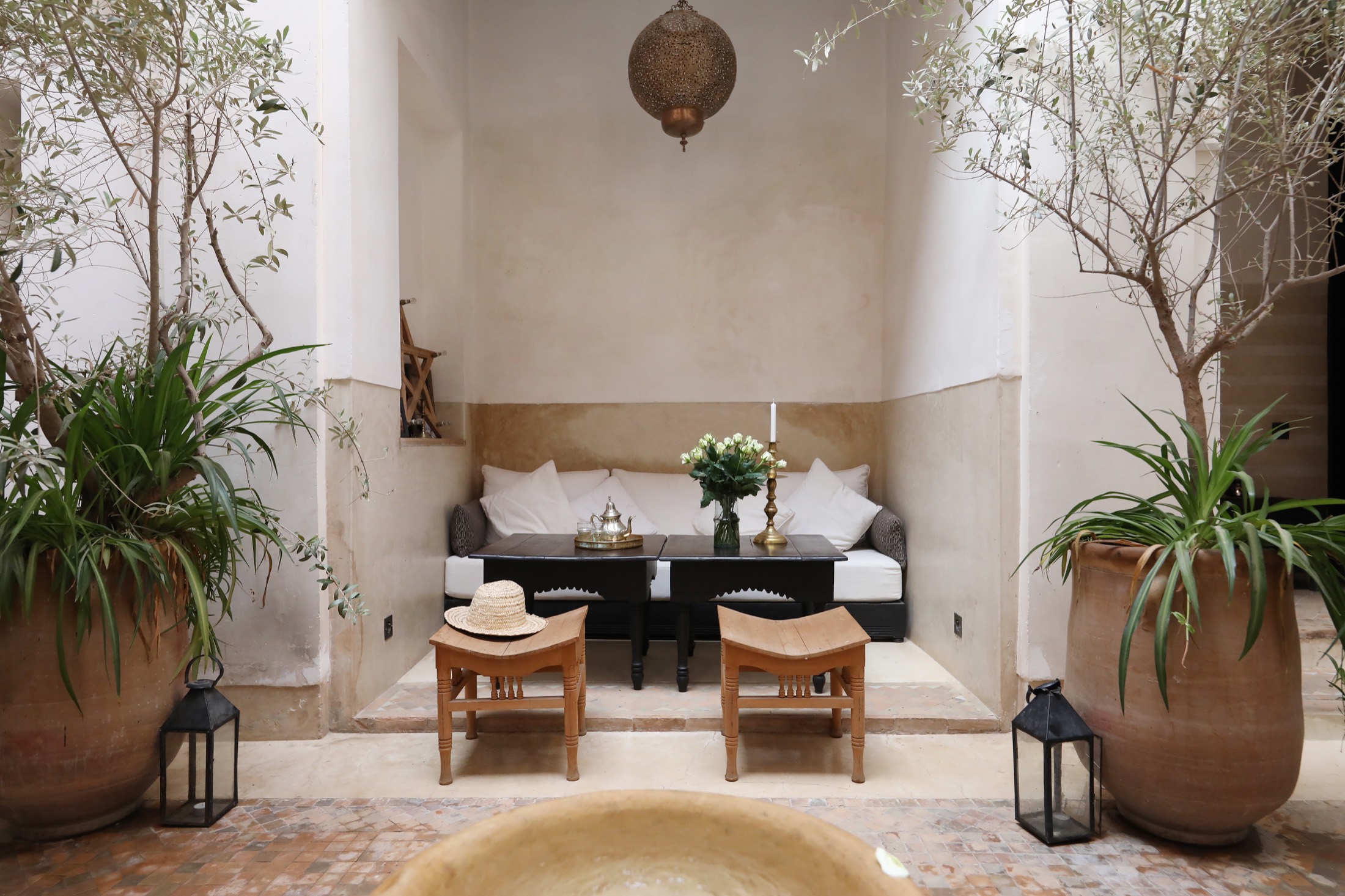 Le patio du Riad Azzouna 13 — banquettes blanches, lanterne ciselée et oliviers en pots, la fontaine au premier plan