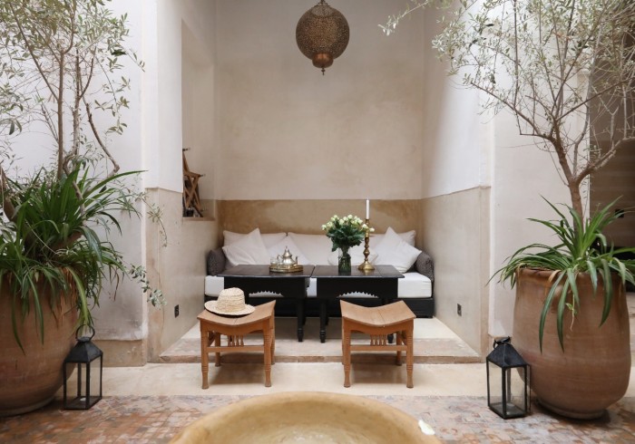 Le patio du riad — banquettes blanches et table basse noire sous le bhou, oliviers en pots