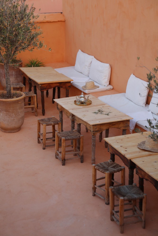 Les tables de bois de la terrasse &mdash; théière de laiton, tabourets de paille et banquettes blanches