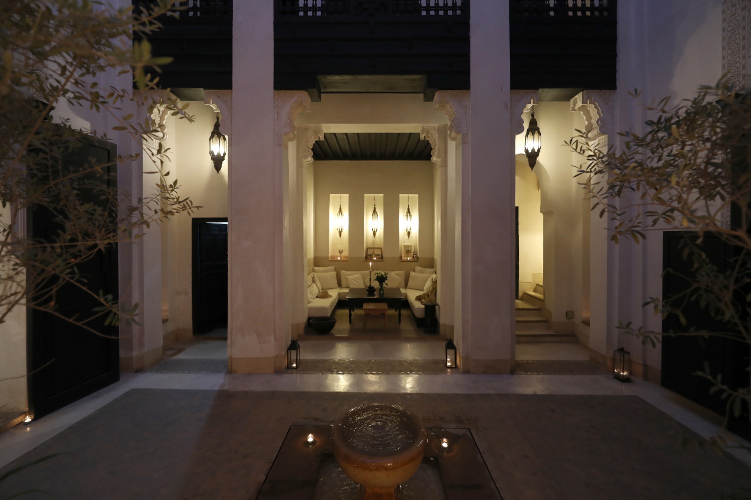 L'enfilade de colonnes du Riad Azzouna 13 à la nuit tombée, la fontaine au premier plan et le salon éclairé
