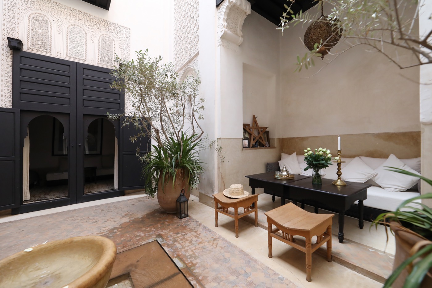 Le patio du riad — les portes de cèdre à moucharabieh, le stuc sculpté et la fontaine, sous les oliviers en pots